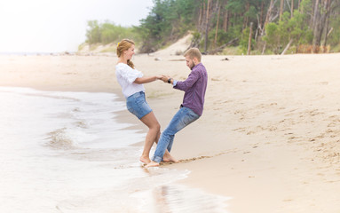 Young couple in love walking along the sea on the beach holding hands and hugging on summer evening
