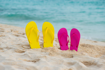 Yellow and pink sandals stand in the sand against the background of the sea.