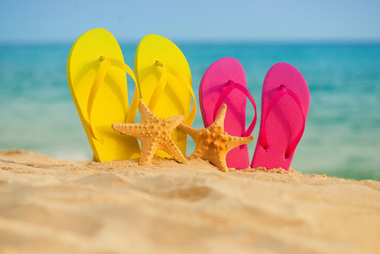 Sea-stars with yellow and pink sandals stand in the sand against the background of the sea.