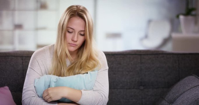 Sad young woman sitting on the couch holding a pillow in front of her