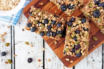 Superfood breakfast bars with oats and blueberries on wood board, overhead scene on rustic...