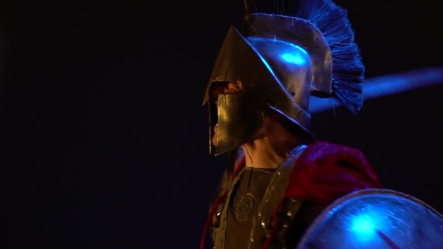 Roman Legionnaire in helmet and armor, falls into a rage, shields behind and beats sword, a bit slow motion