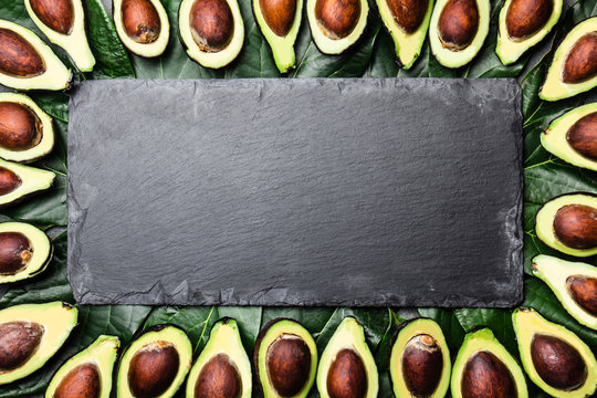 Avocado. Frame made from avocado palta and avocado tree leaves around slate board. Guacamole ingredients. Healthy fat, omega 3. Half of avocado. Top view. Copy space.