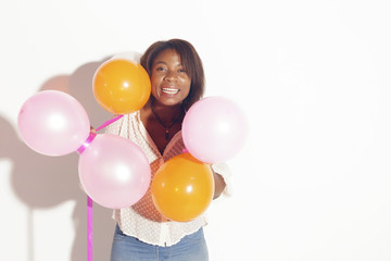 Fototapeta na wymiar Happy african woman holding balloons, smiling to the camera. Over a white background.