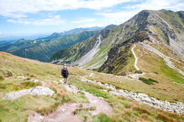 Turysta wędrujący szlakiem w stronę górskiego szczytu.