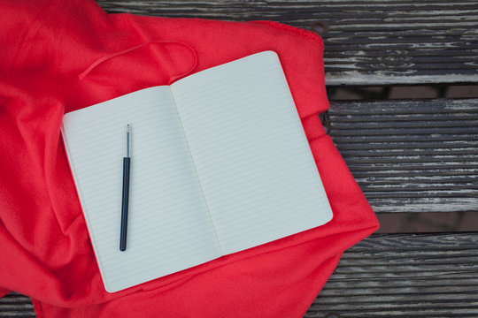 Blank Notepad with a black pen lying on a red blanket. Dark wooden background