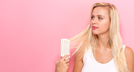Beautiful woman holding a hairbrush on a pink background