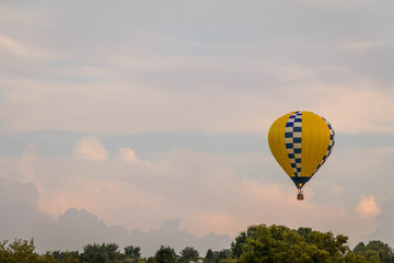 Fototapeta premium Yellow and blue patterned hot air balloon floats among the mountains in a beautiful sky at dusk