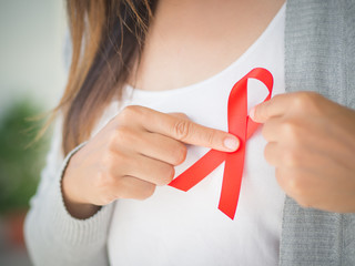 Closeup woman hand holding red AIDS awareness ribbon. Healthcare and medicine concept.