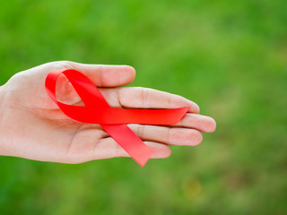 Closeup woman hand holding red ribbon HIV, world AIDS day awareness ribbon.  Healthcare and medicine concept.