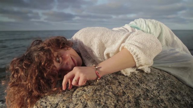 Red-haired girl is lying on a large rock on the beach.
