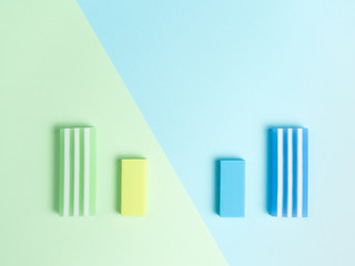 big and little green eraser and blue eraser on green and light blue background.