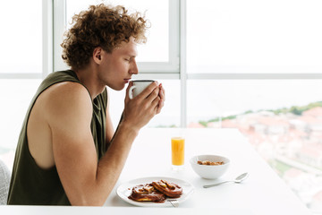 Handsome man sitting at the kitchen and drinking coffee