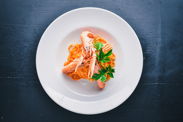 Pasta and tiger shrimp in tomato sauce. Italian traditional food. On a wooden background. Top view. Free space for your text.