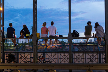 Naklejka premium Young couples in love on romantic date sitting on railway bridge with a bottle of wine and watching the sunset over Munich urban city center. Just the two of us.