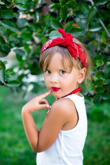 Portrait of cool little girl outdoor near rowan bush. Child in white t-shirt, jeans shorts, red necklace and bandage on the head. Summer.