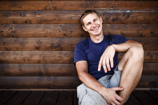 Young Man Sitting And Relaxing On Wooden Deck Outdoor.