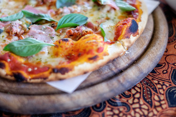 Closeup shot of slices of cheese pizza with dough crust, cheese, bacon, basil and pizza sauce on paper and wooden pan for concept of fast food. Selective blur effect.
