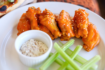 Buffalo wings / barbecue chicken wings on white dish with celery and white dip sauce as side dish for pizza. Closeup view.