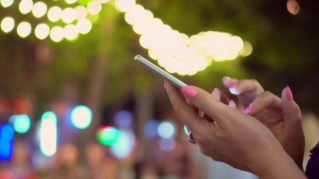 The woman holds the smartphone in hand on the street of the night city. Close-Up Woman Using Smart-Phone In The City