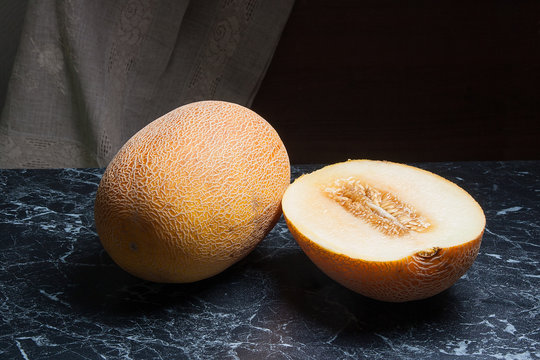 Whole and half honeydew melon fruit on dark marble background.