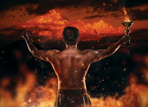 Muscular man holding burning trophy cup, looking at high mountain peak.
