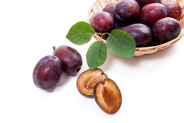Yellow wooden basket with ripe plums, whole and half ripe plums isolated on a white background..