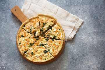 Pie ( quiche) with salmon, spinach and soft cheese on a grey stone background