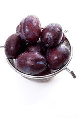 Steel colander with ripe plums isolated on a white background..