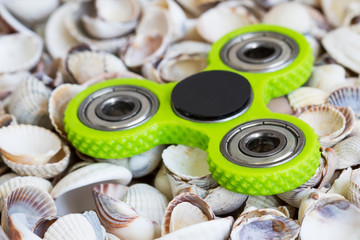 Fidget spinner lies on sea shells. Closeup. Selective focus.