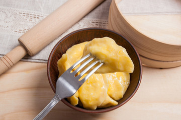Close up view of boiled varenyky or dumpling with cottage cheese or curd on metal fork. Fresh boiled homemade ukrainian dumplings in clay bowl on wooden background..