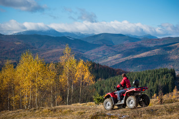 Guy riding on an ATV on the hilly road on a background of mountains, forest and blue sky in the autumn. The concept of an active holiday in the mountains © anatoliy_gleb