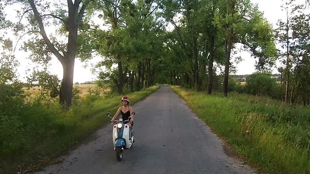A girl is riding a moped on an alley with trees