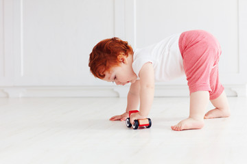 cute redhead baby boy rolling a toy car on the floor