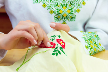 Hands of woman / female / girl in traditional ukrainian shirt sewing ornament of flower dress for...