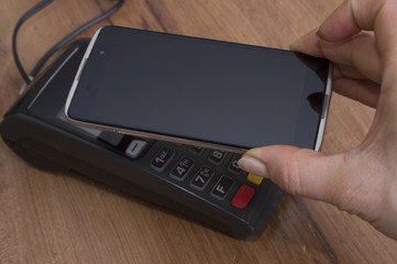 People and modern technology concept. Close up of businessman's hand holding copy space smart hpone close to POS-system while paying for bill after lunch at restaurant.