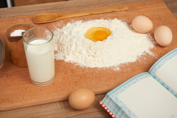 Flour and broken egg closeup for baking on a wooden background. Raw food and kitchen utensils.