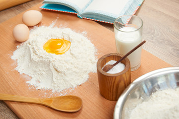 Flour and broken egg closeup for baking on a wooden background. Raw food and kitchen utensils.