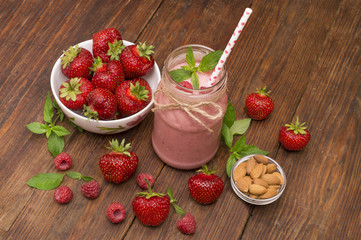 Pink strawberry and raspberry smoothie in a mason jar glass with straw and scattered berries