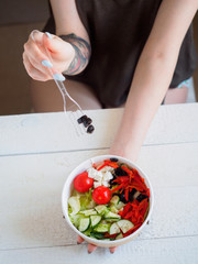 Cardboard container with greek salad in arms