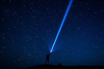 Stars in the sky. The traveler looks at the starry sky. Night sky with stars and silhouette of a man with raised-up arms. The man with the lantern. A strong beam of light. Powerful flashlight