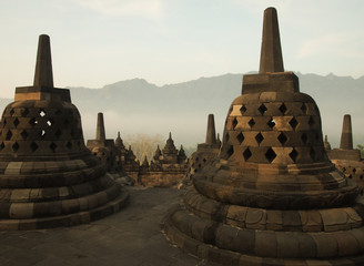 An old stone Buddha statue is placed in a pagoda in Borobudur Temple. It is the world's largest Buddhist temple and is a destination landmark for travel trips in Java, Indonesia.