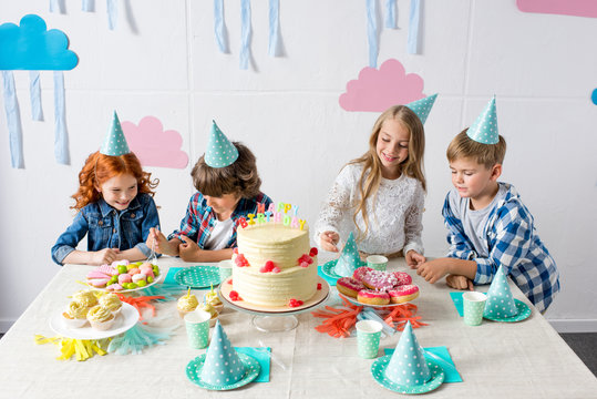 Cute Smiling Kids Eating Sweets While Sitting Together At Birthday Table