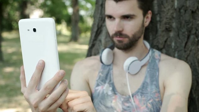 Handsome man doing selfies on tablet in the park, steadycam shot
