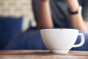 Closeup image of a woman sitting in cafe with white ceramics cup of hot coffee on vintage wooden table in cafe