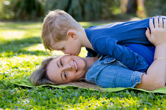 Young son kissing Mother whilst playing on rug in park