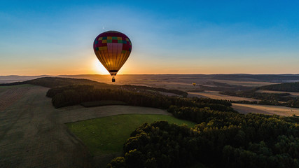 Aerial view of the countryside with a flying balloon in the backlight of the setting sun.