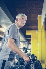 Active senior man lift weights at the gym. Man workout in gym.