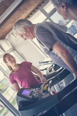 Obraz premium Personal trainer exercise helps elderly couple. Senior couple on the jogging machine.