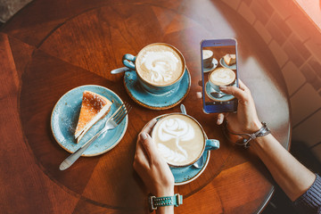 Close-up of mobile smart phone in female hands at the cafe with cup of coffee and cake, flat top view